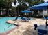 Inviting outdoor pool area with blue loungers and umbrellas, surrounded by lush greenery and modern apartment buildings.