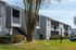 Charming apartment complex with modern gray exterior, lush green landscaping, and a peaceful ambiance.