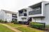 Charming apartment complex with modern gray siding and private balconies, surrounded by lush greenery and manicured paths.