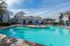 Inviting apartment complex with a sparkling swimming pool, comfortable lounge chairs, and stylish outdoor seating under blue umbrellas.