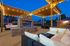 Charming outdoor lounge area featuring cozy sofas under a wooden pergola adorned with twinkling string lights, perfect for evening relaxation.