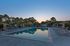 Inviting swimming pool area at sunset, surrounded by lush trees and comfortable lounge chairs, perfect for relaxation and leisure.