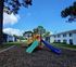 Charming apartment complex with vibrant playground amidst lush greenery under a clear blue sky, perfect for families.