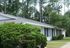 Charming one-story white home surrounded by lush greenery and towering trees, offering a serene and private atmosphere.