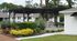 Charming outdoor patio with a stylish black pergola surrounded by lush landscaping, highlighting vibrant flowers and manicured shrubs.