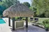 Inviting outdoor area featuring a charming thatched-roof cabana beside a sparkling pool, surrounded by lush greenery and cozy seating.