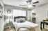 Bright and cozy bedroom with elegant decor, featuring a plush bed with stylish cushions, a charming lamp, open closet, and modern ceiling fan.