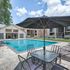 Inviting apartment complex featuring a pristine swimming pool, shaded seating area, and modern building exteriors, perfect for relaxation and leisure.