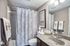 Inviting bathroom with elegant decor, featuring a modern vanity with speckled countertop, stylish lighting, and artistic shower curtain creating a cozy ambiance.