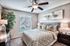 Inviting bedroom with chic decor, featuring a cozy bed with patterned pillows and a stylish ceiling fan, complemented by warm lighting and elegant furnishings.