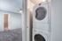 Modern apartment with built-in washer and dryer in a cozy laundry area, adjacent to a spacious carpeted room.