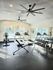 Modern apartment gym with state-of-the-art fitness equipment, featuring treadmills, exercise bike, weight bench, and dumbbell rack under stylish ceiling fans.