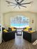 Bright and inviting lounge area with modern wicker chairs, vibrant yellow cushions, and large windows overlooking a serene pool.