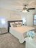 Inviting bedroom with plush carpeting, stylish bed with gray headboard, elegant nightstands, and ceiling fan; perfect retreat for relaxation.