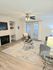 Chic modern living room with elegant decor, featuring a plush gray sofa, stylish glass coffee table, and large window with white drapes, illuminated by a sleek ceiling fan light.