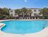 Inviting apartment complex with a crystal-clear pool surrounded by palm trees and lounge chairs, offering a relaxing tropical ambiance.