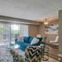 Elegant living room with a vibrant blue sofa, stylish zigzag-patterned chair, and plush white rug, leading to a balcony with scenic views.