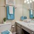 Modern bathroom with elegant fixtures, chic blue towels, decorative plants, and a well-lit vanity mirror.