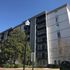 Modern apartment building with balconies, surrounded by lush greenery and a clear blue sky.