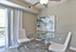 Modern dining area with elegant round glass table and stylish white chairs, featuring a contemporary abstract painting and ample natural light from the sliding glass door.