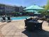 Luxurious apartment complex featuring a sunlit pool area with elegant lounge chairs and stylish outdoor seating under large umbrellas.