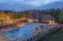 Inviting evening view of a luxurious swimming pool and clubhouse, surrounded by lush greenery and ambient lighting.