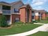Charming brick apartment complex with lush greenery and private balconies under a bright blue sky.