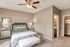 Inviting bedroom featuring a sleek ceiling fan, cozy bed with plush pillows, mirrored nightstands, and soft carpet flooring.