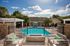 Charming community pool area featuring cozy seating, sunny blue sky, and lush greenery, perfect for relaxation and outdoor enjoyment.