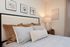 Elegant bedroom with a cozy bed, stylish artwork, and a warm ambiance created by a modern table lamp.