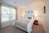 Inviting bedroom with a large window, plush bed adorned with soft pillows, elegant lampshades, and nature-themed artwork.