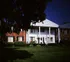 Charming apartment building with classic white pillars, surrounded by lush greenery and vibrant flowers.