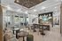 Modern, elegant communal lounge with a stylish dining area, wood accents, and chic lighting, offering a seamless view of the poolside through large glass doors.