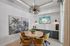 Elegant dining area with a round wooden table, stylish mustard chairs, tropical artwork, and a modern light fixture, featuring coastal artwork on a screen.