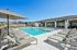 Luxurious apartment complex pool area featuring a sparkling swimming pool, sun loungers, and shaded seating under a clear blue sky.