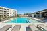 Luxurious apartment complex with a sparkling swimming pool, surrounded by modern lounge chairs and stylish buildings under a clear blue sky.