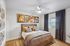 Chic bedroom with modern decor, featuring abstract art, plush bedding, and a sunlit window with elegant curtains.