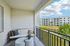 Charming apartment balcony with cozy seating and scenic view of lush greenery and modern building complex.