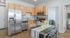 Modern kitchen with sleek stainless steel appliances, warm wood cabinetry, and a stylish dining area with a plant centerpiece.