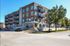 Modern apartment building with spacious balconies and a sleek brick design, set in a vibrant neighborhood with lush trees and convenient street access.