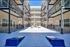 Modern apartment courtyard featuring sleek balconies, a vibrant patio umbrella, and fun cornhole game setup in a sunlit open space.