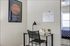 Chic workspace with a glass desk, modern lamp, and a wall calendar, offering a glimpse into a cozy bedroom.