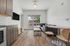 Modern apartment living area with sleek wood flooring, cozy gray sofa, wall-mounted TV, and natural light from a large window.