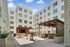 Modern apartment courtyard with stylish seating, barbecue grill, and string lights under a clear blue sky. Inviting outdoor space for relaxation and social gatherings.
