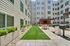 Inviting apartment courtyard featuring lush green space, modern outdoor seating, and sleek barbecue grills for a perfect gathering spot.