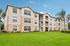 Charming apartment complex with three-story, light-toned building, lush green lawn, and inviting balconies.
