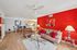 Contemporary living room with vibrant red accent wall, plush seating, and elegant decor, featuring open layout to dining area and kitchen.