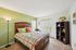Bright and inviting bedroom with stylish green accent wall, modern wooden bed, cozy decor, and ample natural light.
