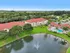 Aerial view of a modern apartment complex with red roofs, lush greenery, and a sparkling pool beside a tranquil pond with a fountain.