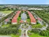 Aerial view of a picturesque apartment complex with red-roofed buildings surrounding a serene lake, lush greenery, and a pristine pool area, ideal for comfortable living.